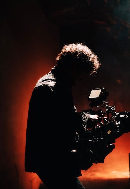 A professional cameraman captures footage in a creatively lit, moody setting, backlit by warm light.