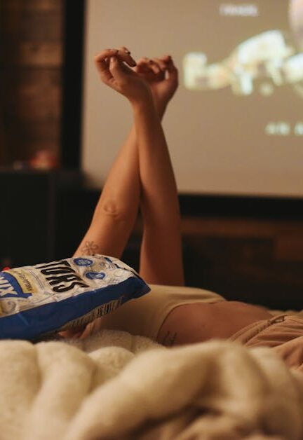 Relaxing movie night at home, lying in bed with snacks and a projector.