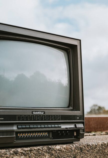 Black old fashioned obsolete television with reflection on screen placed on concrete railing against cloudy ski on street on blurred background