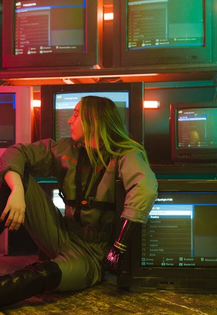 A woman with a prosthetic hand sits in a neon-lit room surrounded by retro TVs.