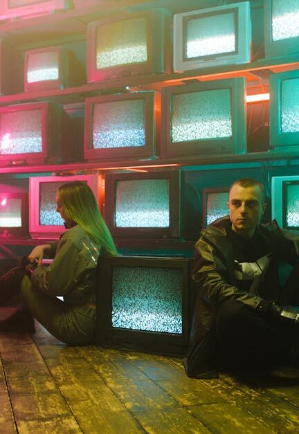 Two individuals in a cyberpunk setting with neon lighting and stacked television screens.